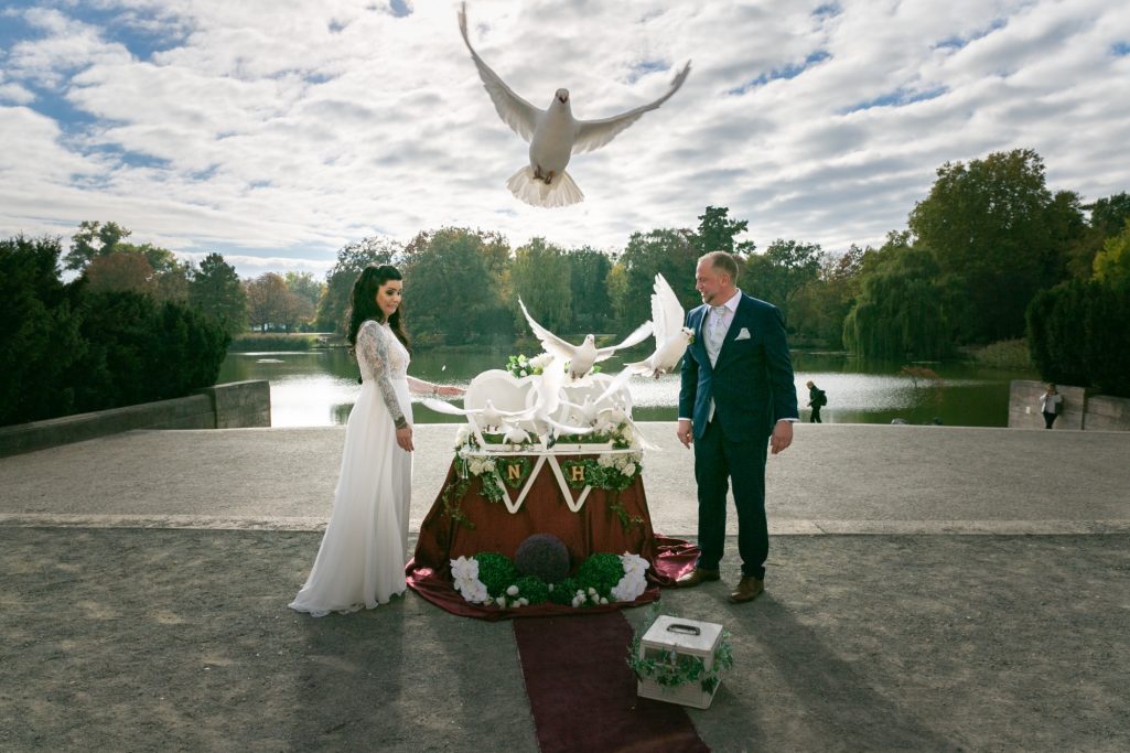 Braut und Bräutigam lassen weiße Tauben in einem Park fliegen.