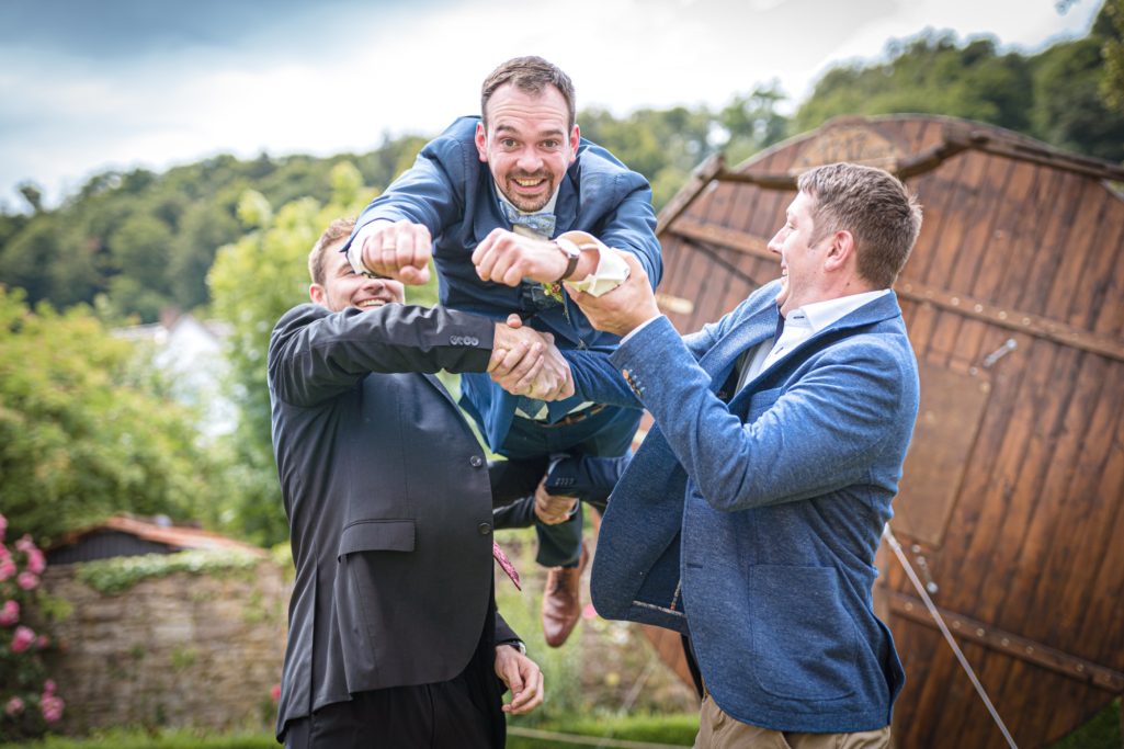 Drei Männer heben einen Freund spielerisch in die Luft und lachen dabei.