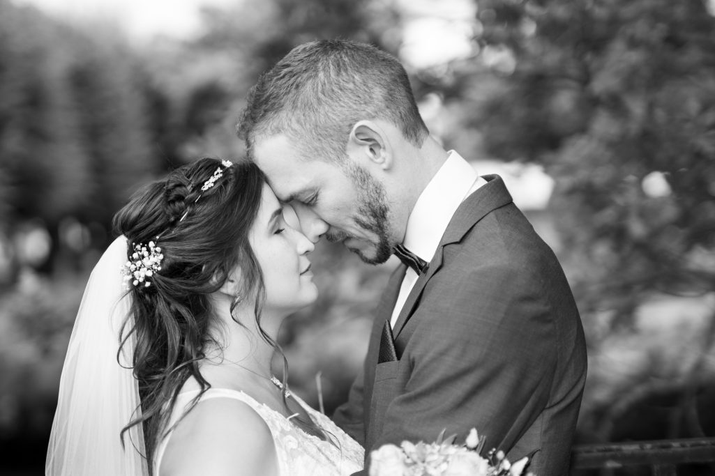 Ein Brautpaar steht sich gegenüber, lächelt und berührt sich sanft mit den Stirnen.