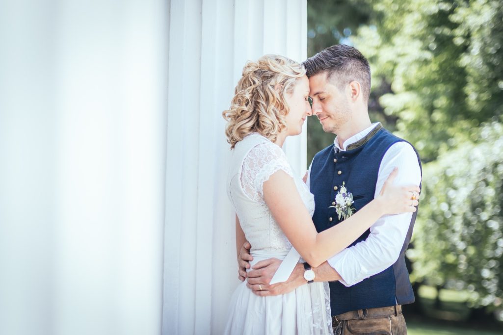 Hochzeitspaar umarmt sich zärtlich vor einer hellen, natürlichen Kulisse.