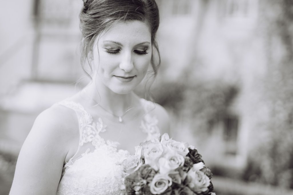 Eine Braut in einem eleganten Kleid hält einen Blumenstrauß und lächelt sanft.