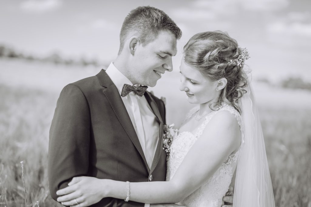 Brautpaar in eleganter Kleidung, lächelnd und umarmend, vor einer weiten, natürlichen Kulisse.