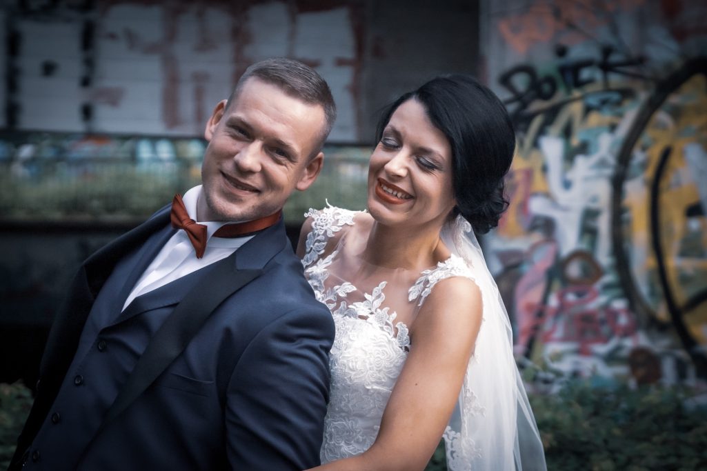 Brautpaar posiert lächelnd vor einer bunten Graffiti-Wand.