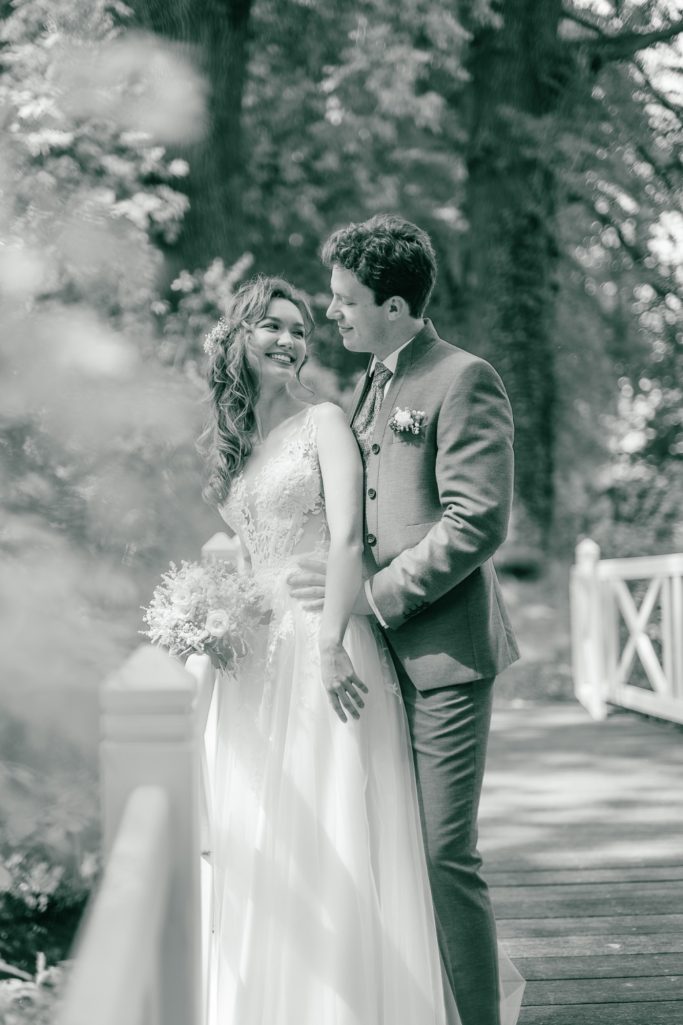 Hochzeitspaar auf einer Brücke umgeben von Bäumen, in sanften Grautönen.