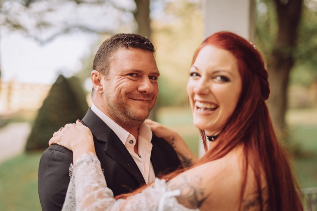 Lächelndes Paar im Freien, Frau mit langen roten Haaren und tätowierten Armen.