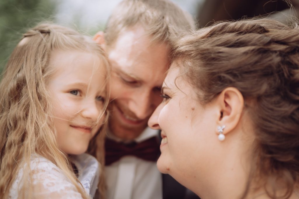 Eine Familie mit Vater, Mutter und Tochter, die einander liebevoll anlächeln.