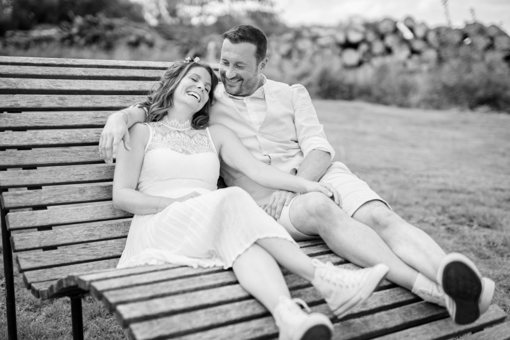 Paar sitzt entspannt auf einer Bank und lächelt, umgeben von Natur.