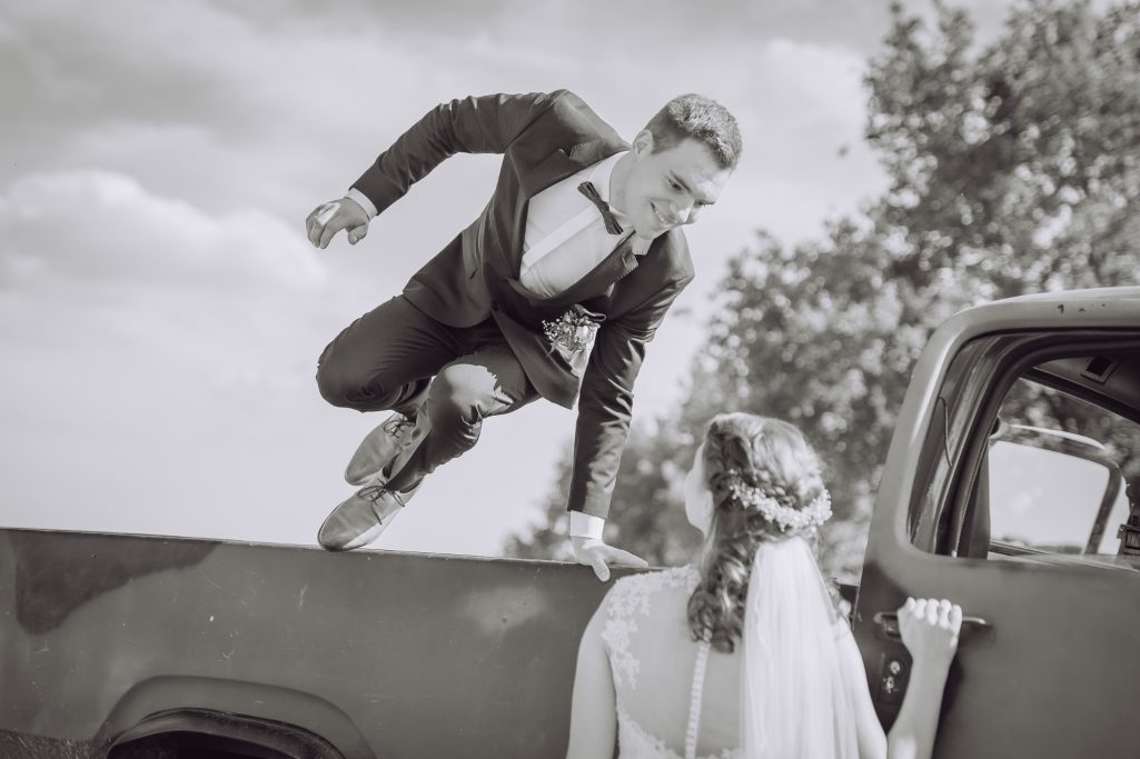 Ein Bräutigam springt von einem Truck zu seiner Braut. Schwarz-weiß-Foto.