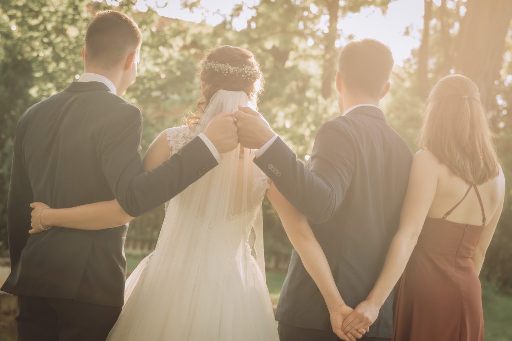 Ein Brautpaar und zwei Begleitpersonen, stehen Rücken an Rücken in der Abendsonne.