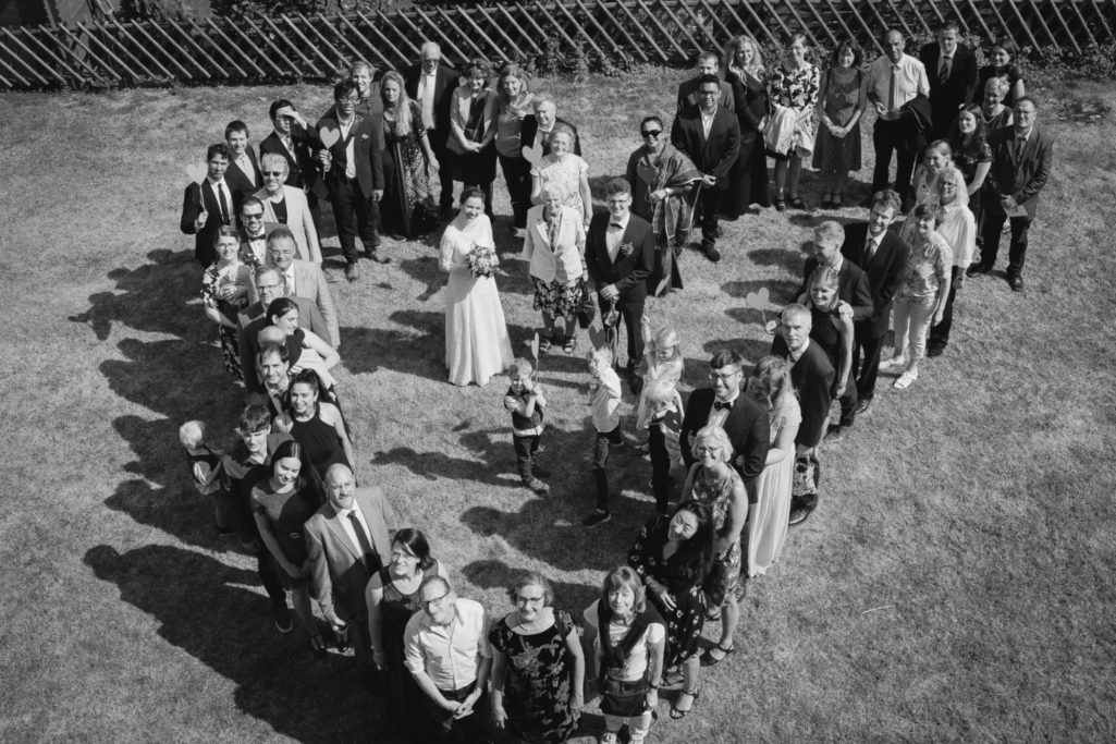 Eine Gruppe von Menschen bildet in einem Garten ein Herz aus Personen.