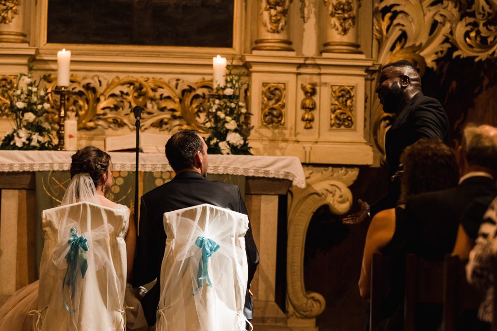 Hochzeitszeremonie mit Paar, das am Altar sitzt, Blumen und Kerzen im Hintergrund.