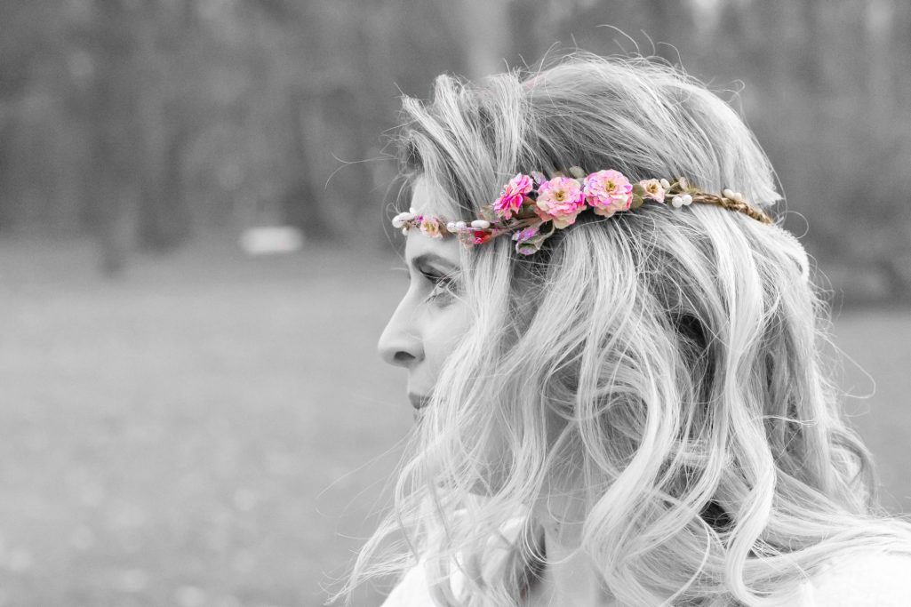 Frau mit blonden, lockigen Haaren und einem Blumenkranz im Profil.